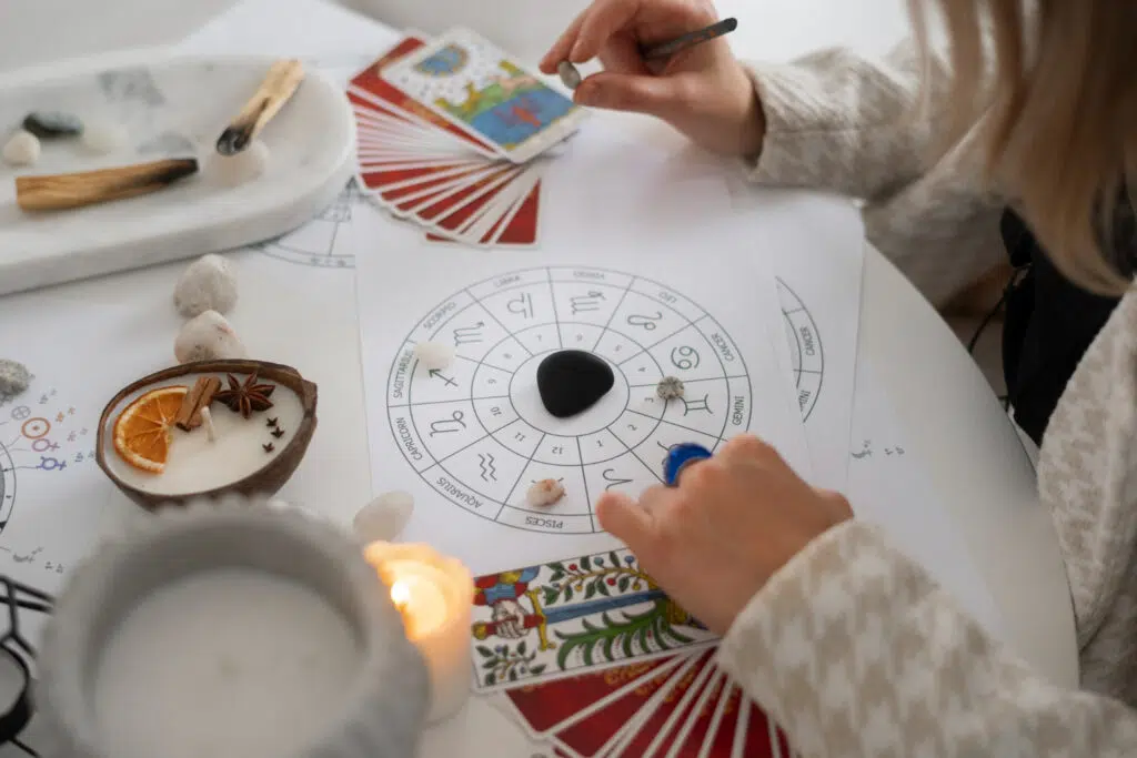 une femme en gros qui tint une pierre au dessus d'un tableau astrologique, posé à côté d'un jeu de tarot, une bougie et de l'encens. 